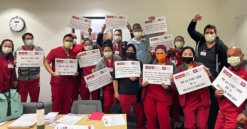 Large group of nurses inside hospital hold signs "Health care is a human right" with raised fists