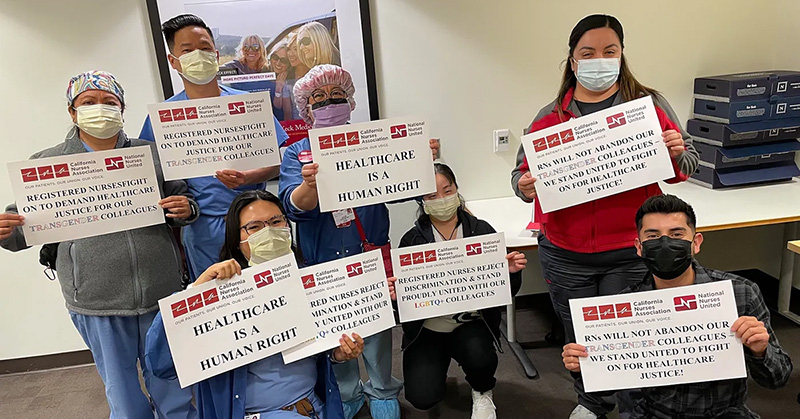 Large group of nurses inside hospital hold signs "Health care is a human right" 