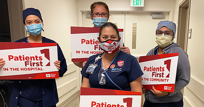 Four nurses inside hospital hold signs "Patients First"
