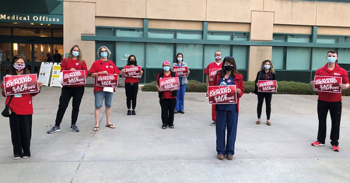 Nurses outside hospital hold signs calling for safe staffing