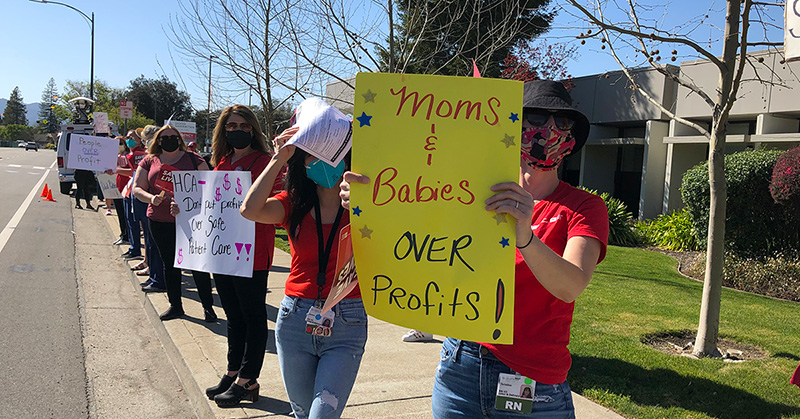 Nurse outside holds sign "Moms & Babies Over Profits"
