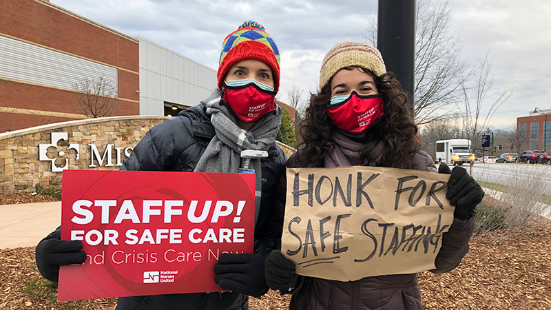 Two nurses outside hospital hold signs calling for safe staffing