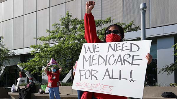 Nurse holds sign "We Need Medicare for All"