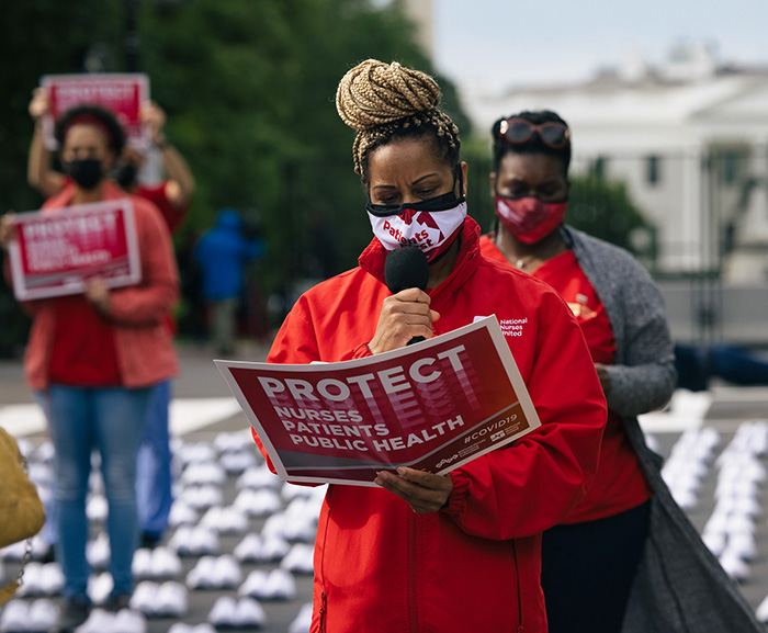 Nurse holds sign "Protect Nurses, Patients, Public Health"