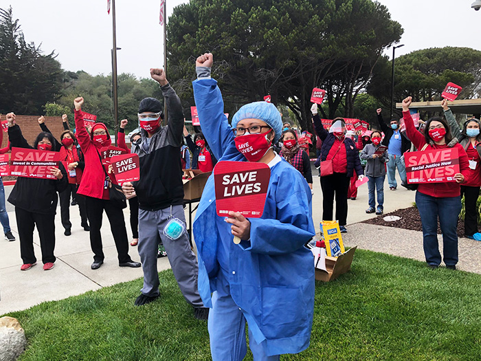 Large group of nurses with raised fists hold signs "Save Lives"