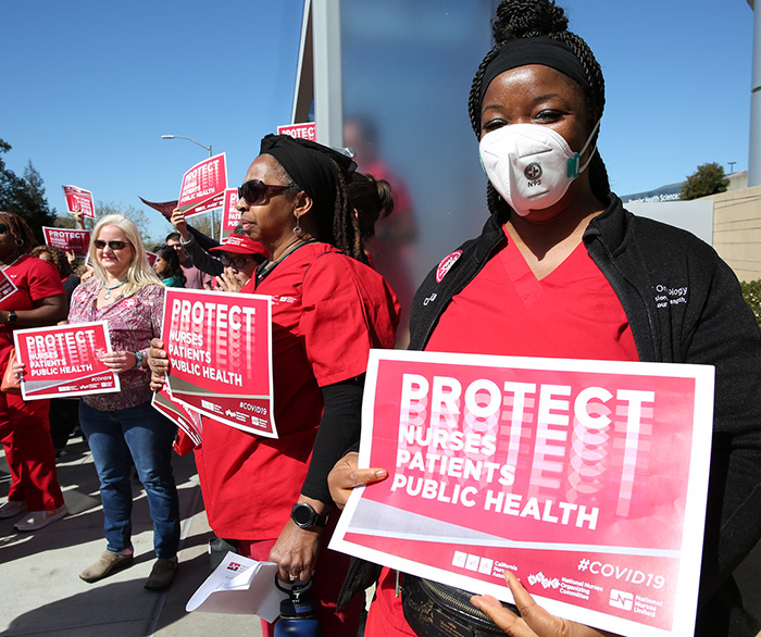 Nurse holds sign "Protect Nurses, Patients, Public Health"