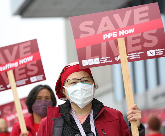 Nurse holds sign "Save Lives: PPE Now"