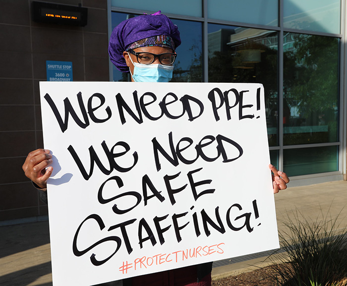 Nurse holds sign "We Need PPE, We Need Safe Staffing"