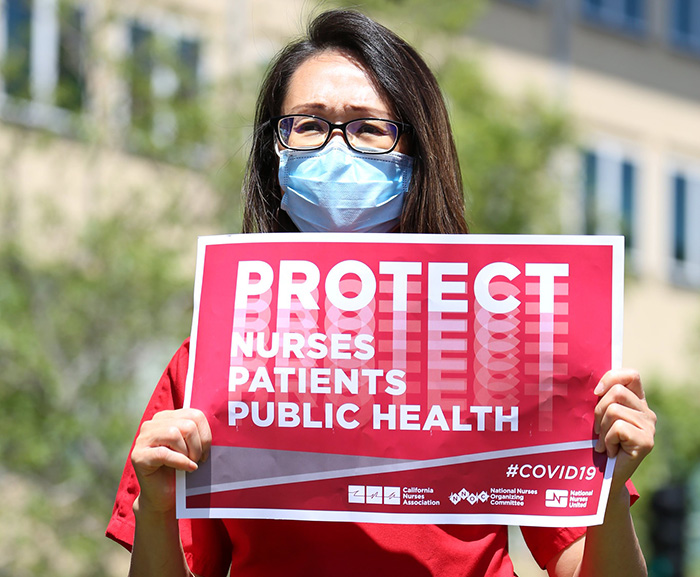 Nurse holds sign "Protect Nurses, Patients, Public Health"