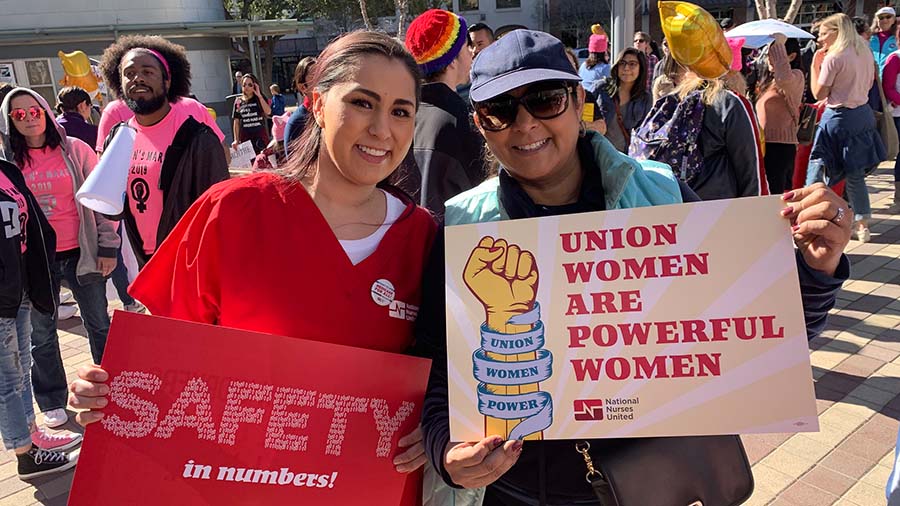Two women hold signs "Union women are powerful women", "Safety in numbers"