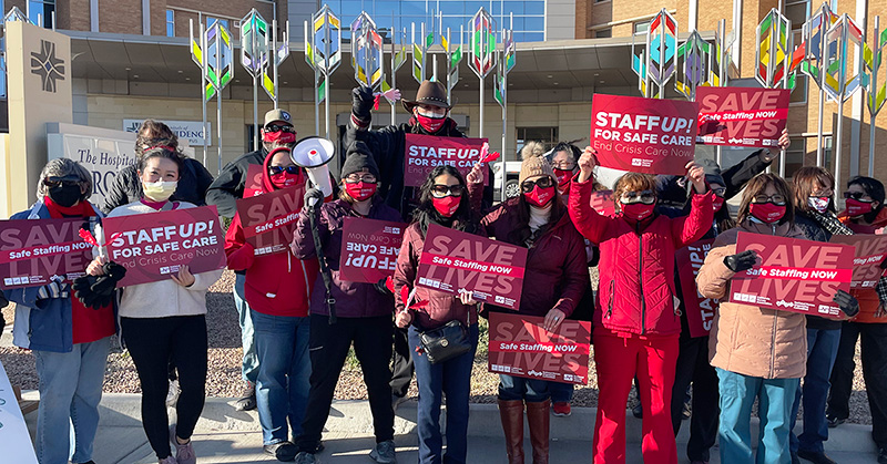 Large group of nurses outside hospital hold signs calling for safe staffing