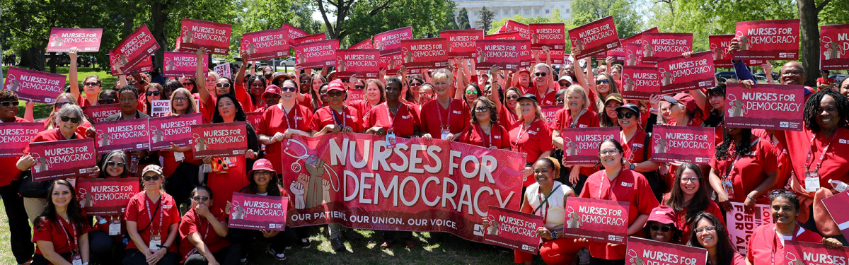 Large group of nurses outside Capitol Building in Washington, D.C. holding signs and banner "Nurses for Democracy"