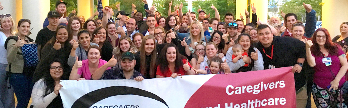 Large group of health care workers outside holding banner: CHEU: Caregivers and Healthcare Employees Union