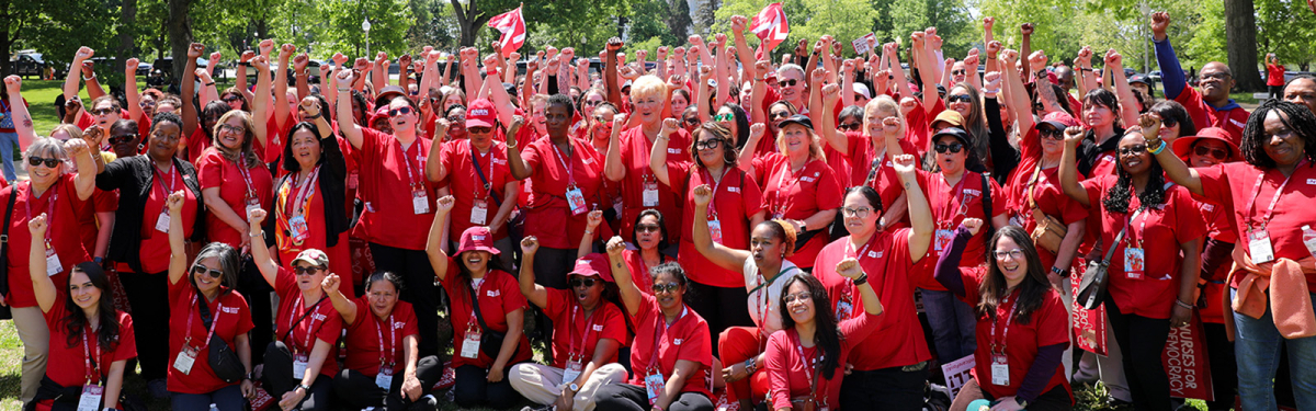 Large group of nurses outside, wearing red, smiling, with raised fists