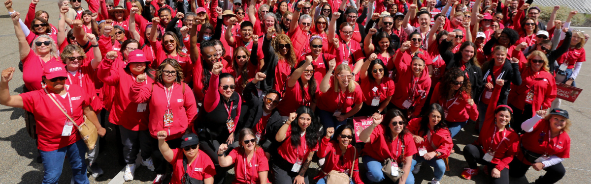Large group of nurses wearing red, with raised fists