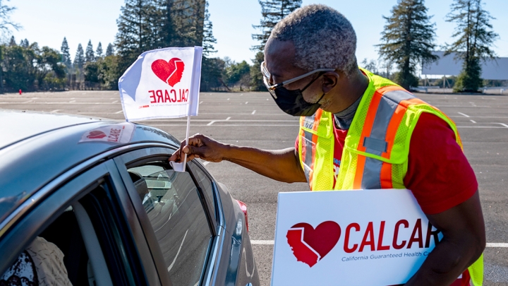 Person holding heart CalCare sign and placing flag on car.