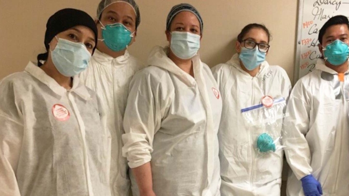 Group of five nurses inside hospital wearing protective gowns