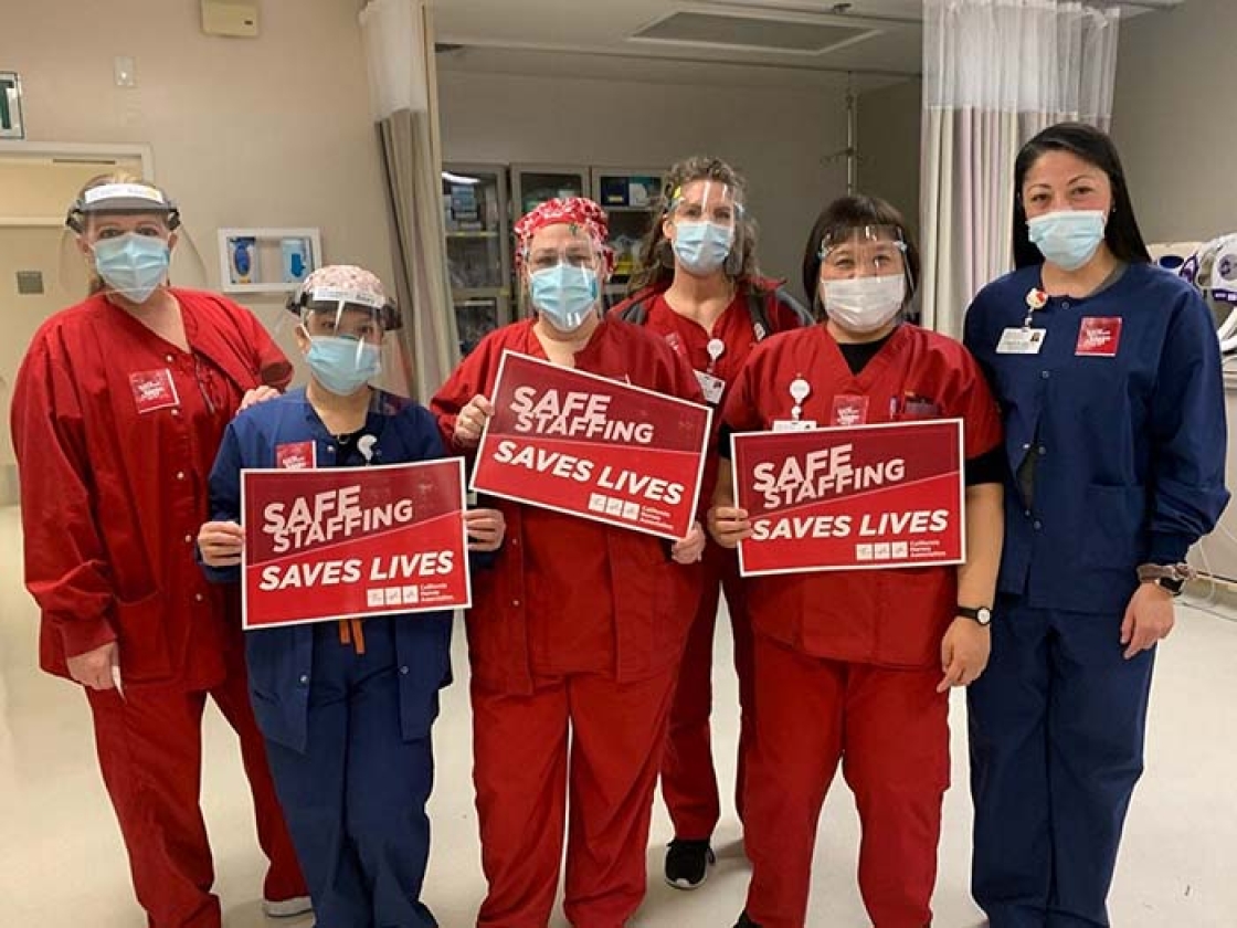 Nurses inside hosptial hold signs "Safe Staffing Saves Lives"