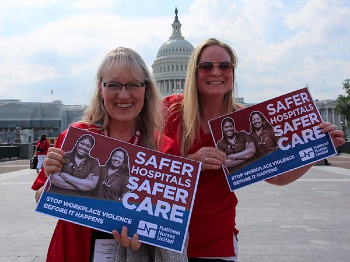 Two nurses outside Capitol building hold signs calling for workplace safety