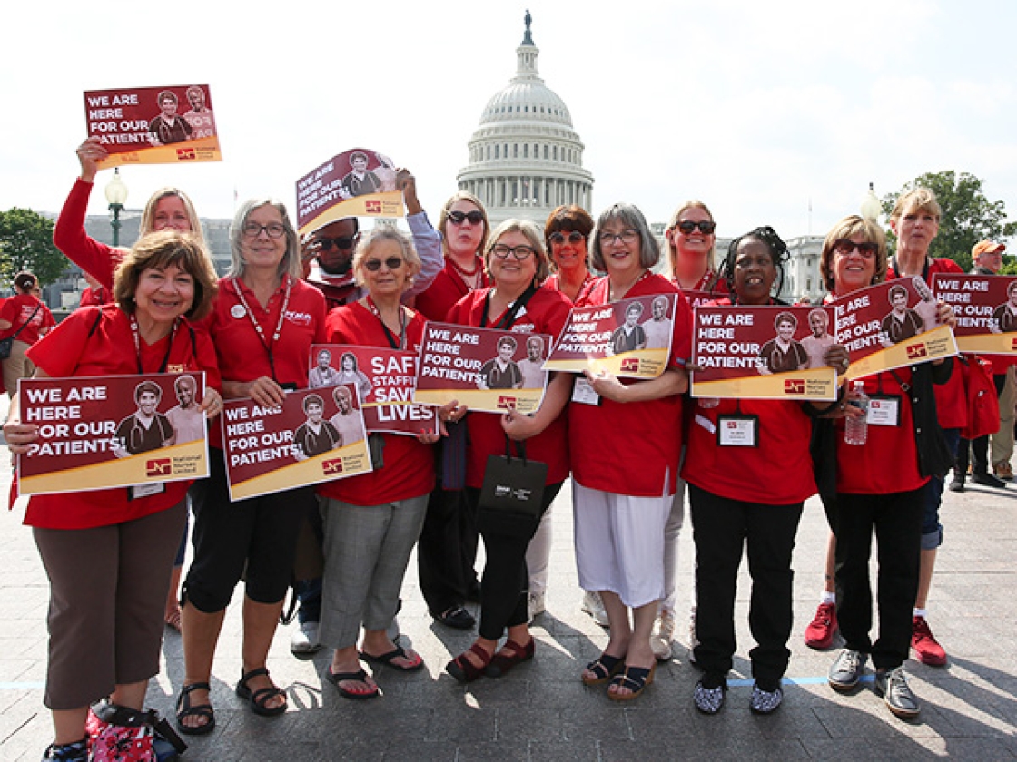 Large group of nurses outside Capitol Building hold signs "We are here for our patients"