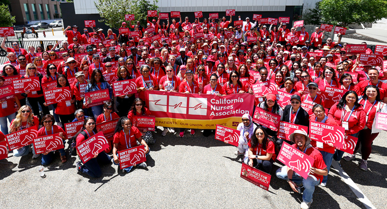 Large group of nurses outside, wearing red CNA shirts, holding banner "California Nurses Association"