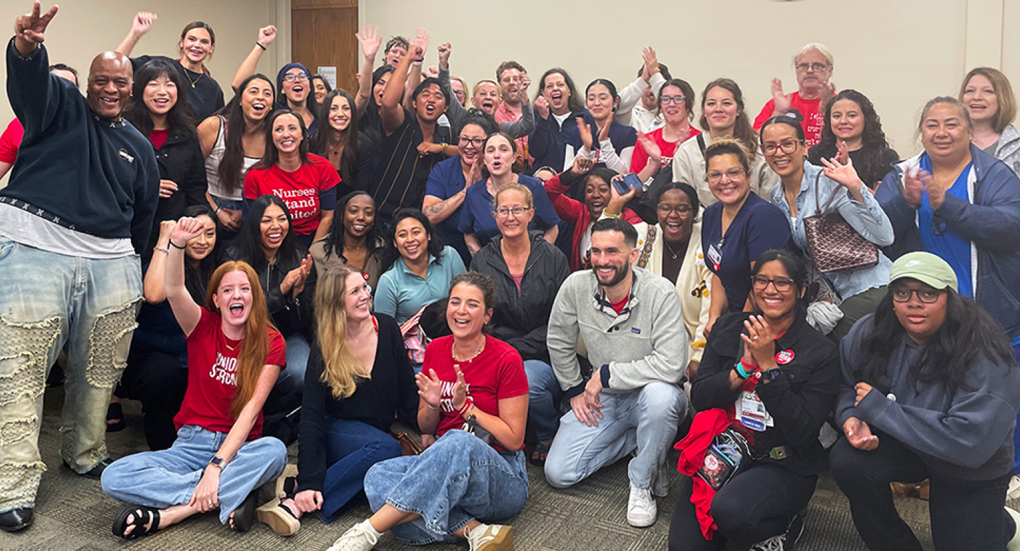 Large group of nurses inside hospital meeting room smiling with raised fists