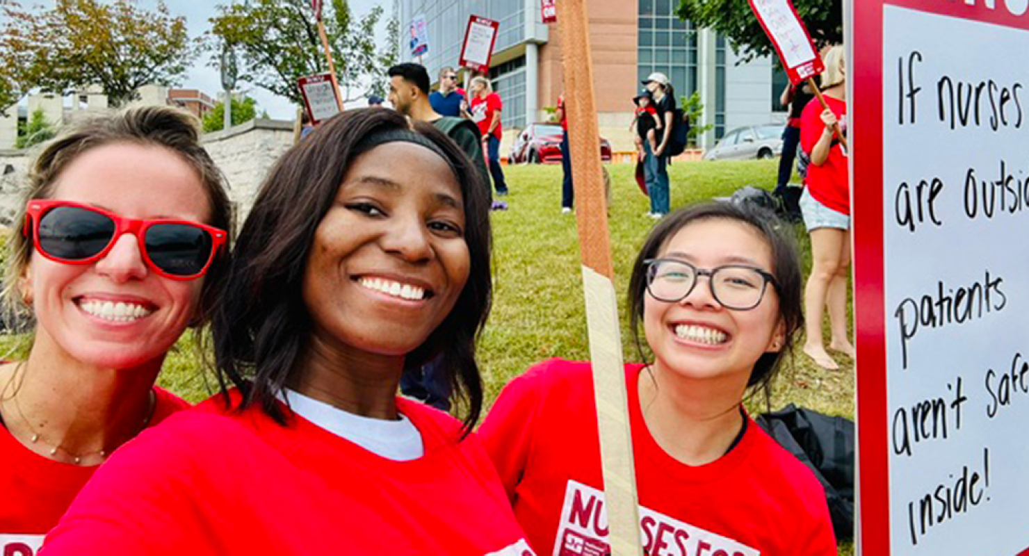 3 nurses outside hospital smiling, wearing red