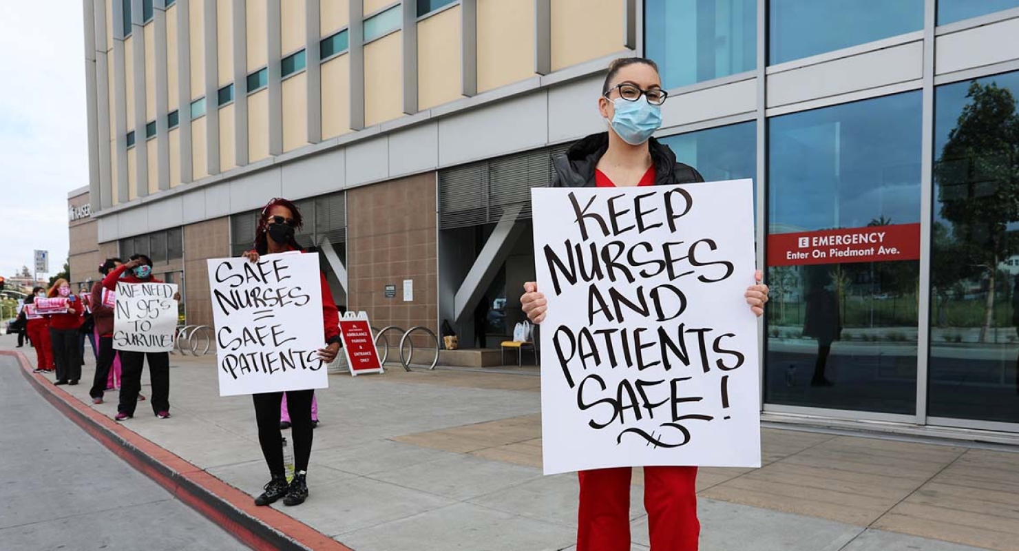Nurses outside hospital hold signs "Keep nurses and patients safe"