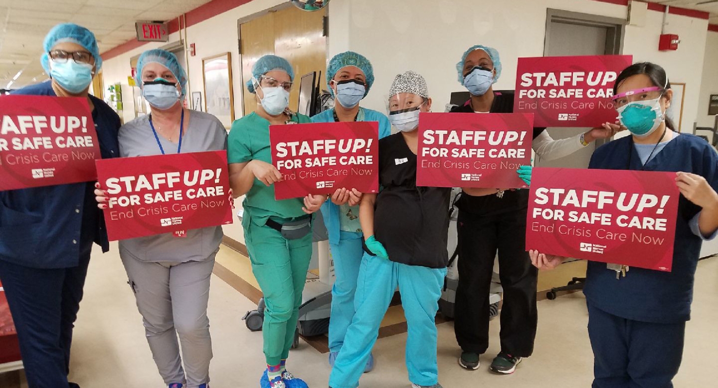 Large groups of nurses inside hospital hold signs "Staff Up for Safe Care"