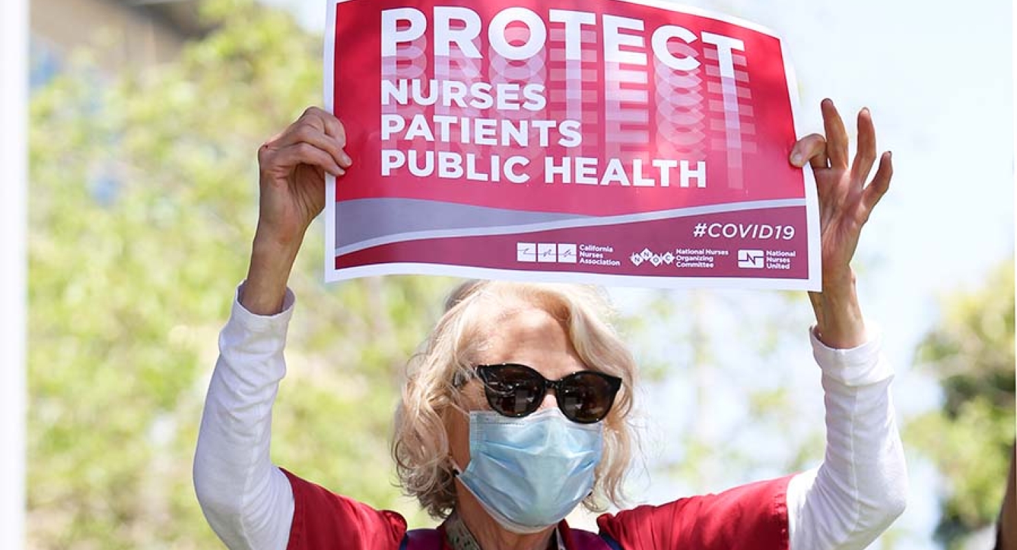 Nurse holds sign "Protect Nurses, Patients, Public Health"