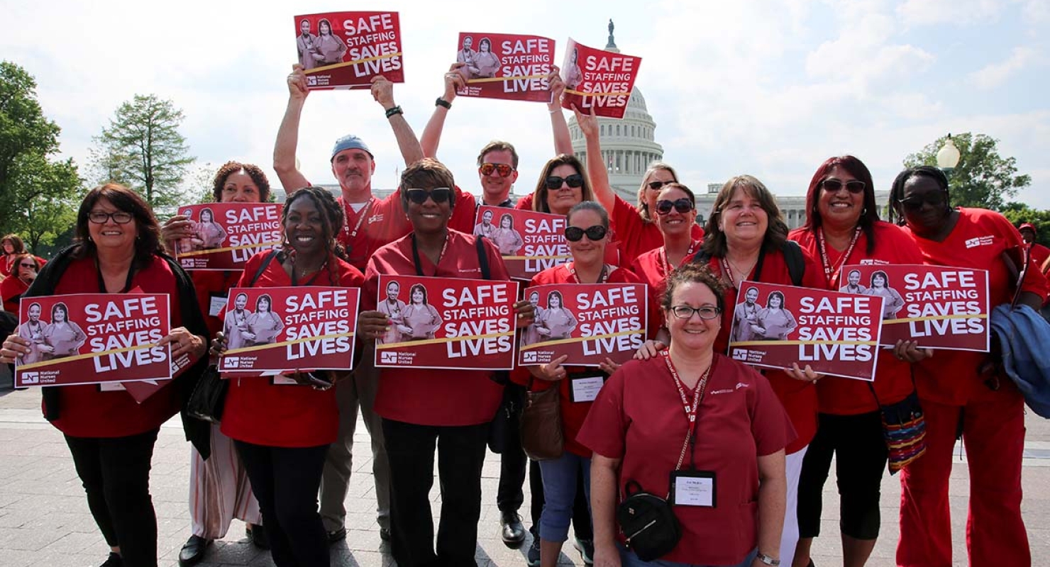 Large group of nurses hold signs "Safe Staffing Saves Lives"