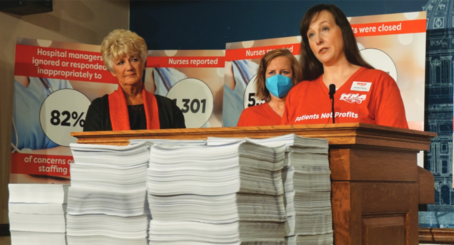 Group of three nurses standing at podium with stacks of paper report