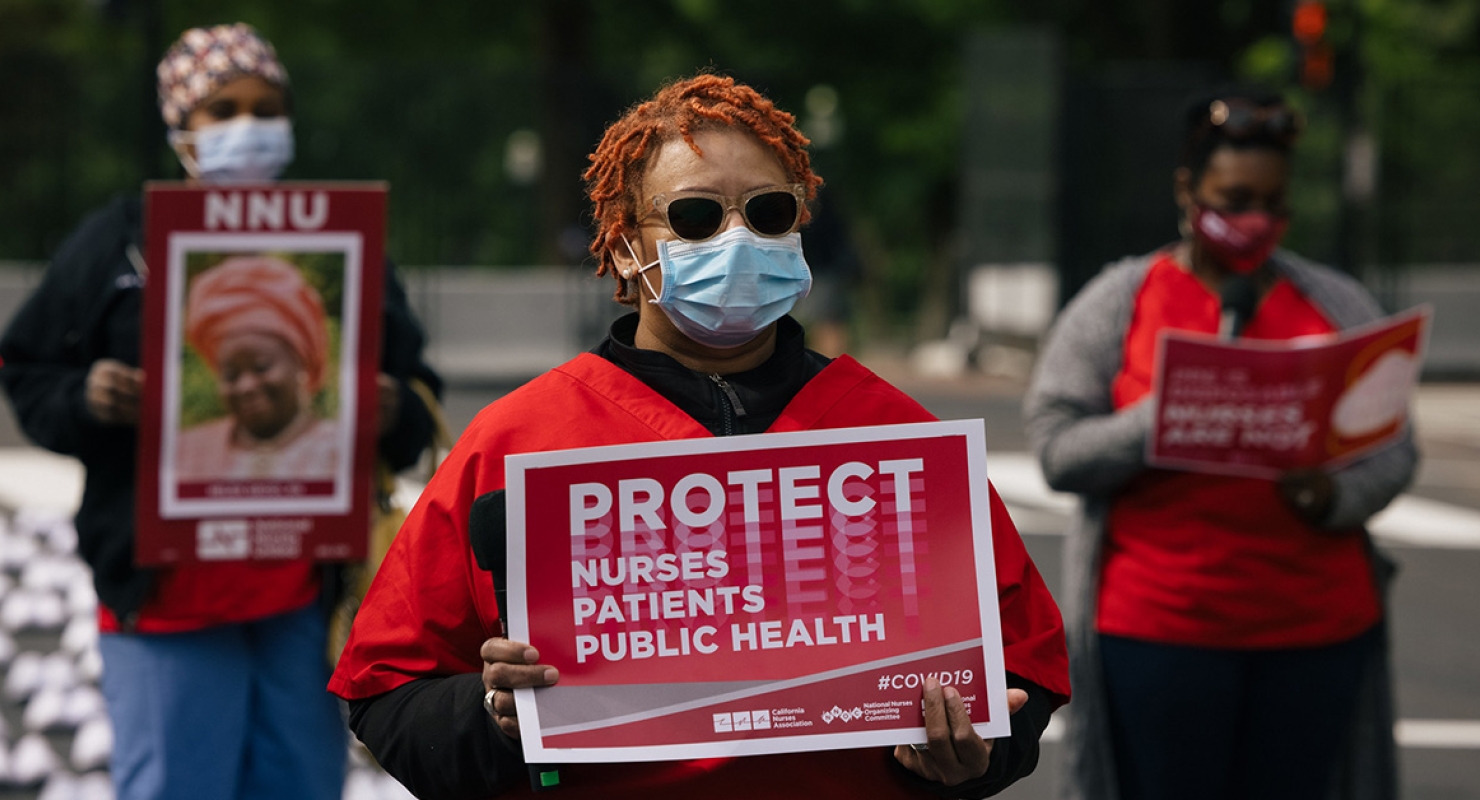 Masked nurse outside holds signs "Protect Nurses, Patients, Public Health"