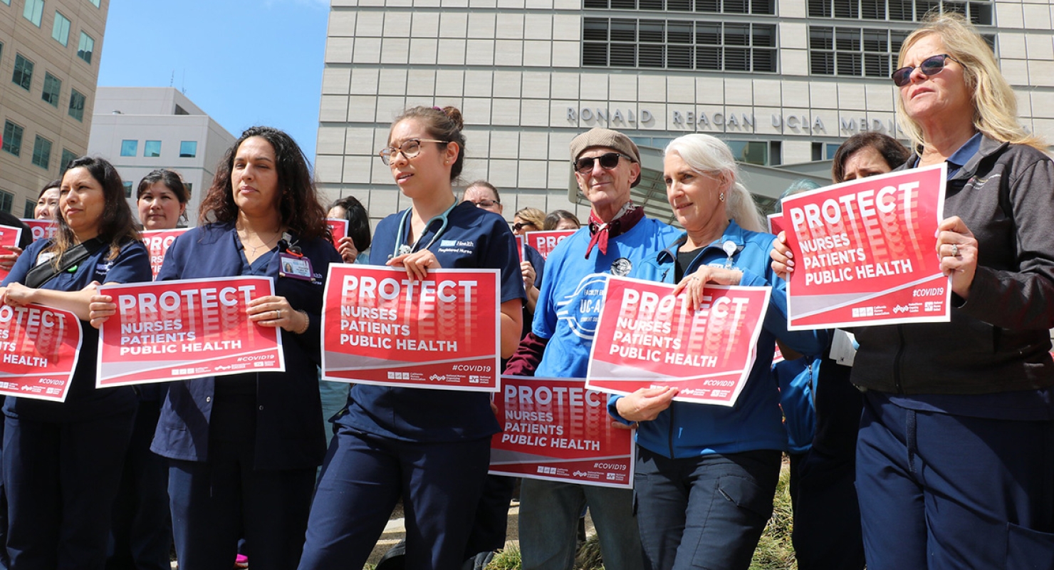 Nurses outside hold signs "Protect Nurses, Patients, Public Health"