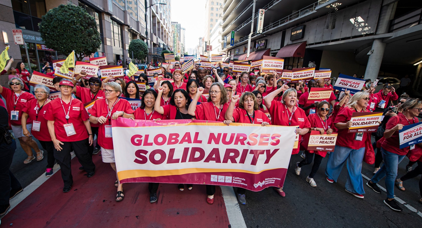 Nurses marching down street holding banner "GLobal Nurses Solidarity"