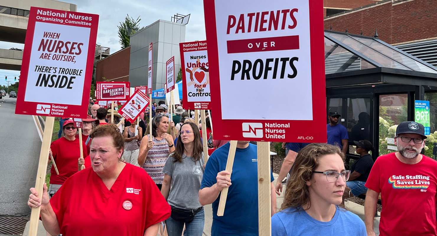 Nurses picketing outside hospital holding signs "Patients over Profits"