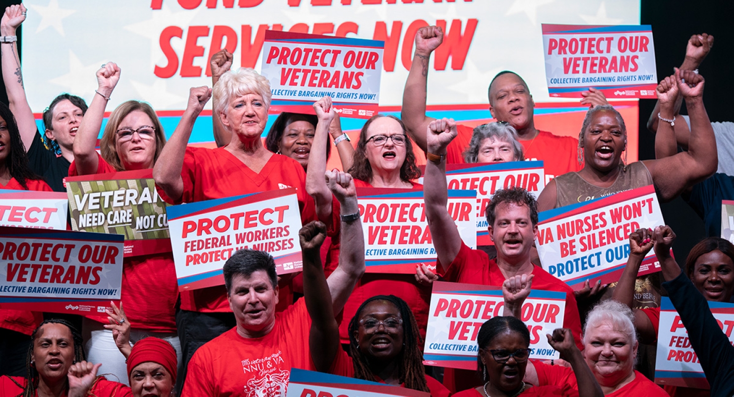 Large group of nurses with raised fists, holding signs "Protect Federal Workers, Protect VA Nurses"