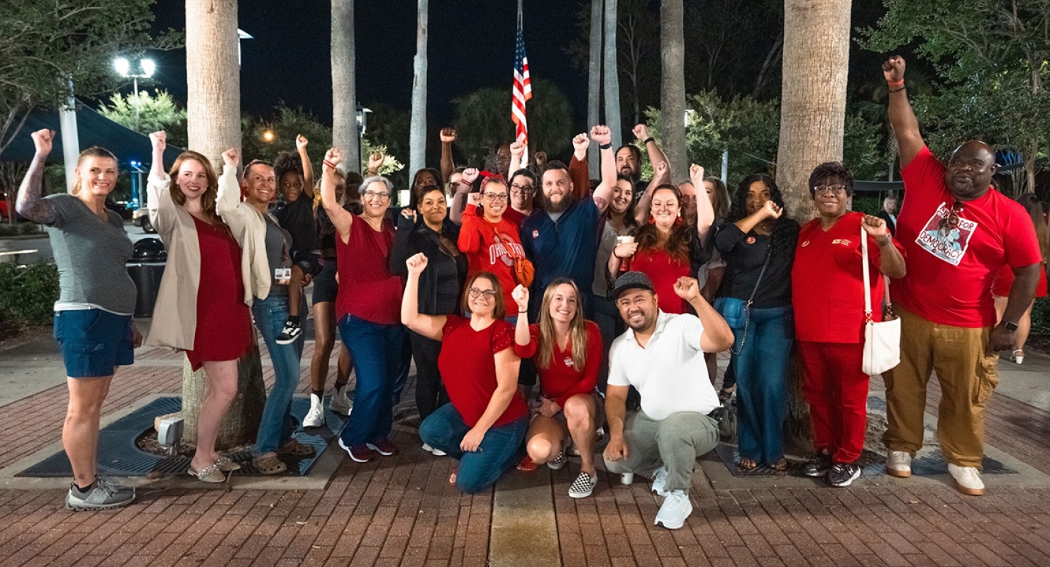 Large group of nurses outside, smiling, with raised fists