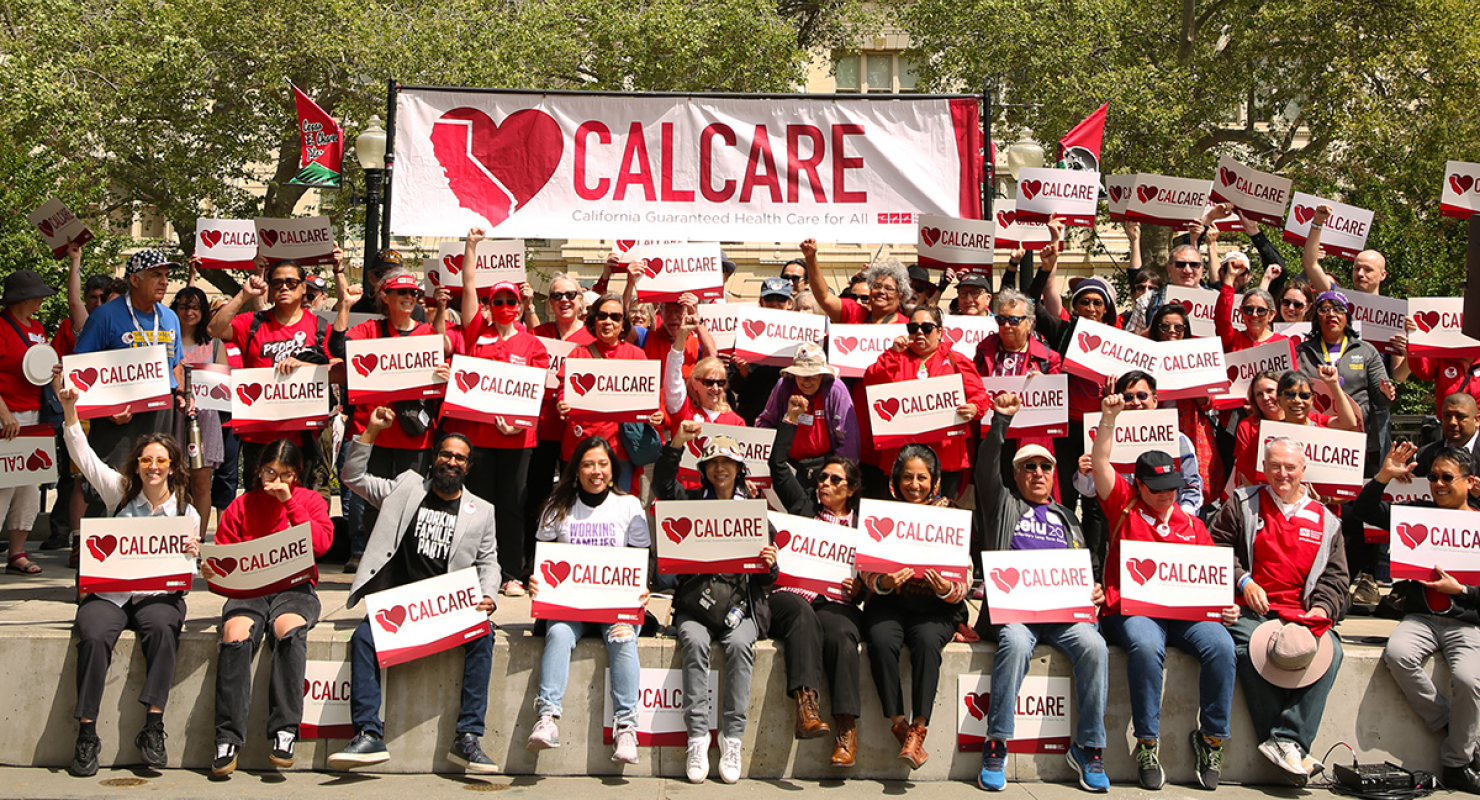 Large group of people outside, smiling, raised fist, underneath "CalCare" banner, and holding "CalCare" signs
