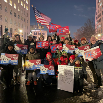 Large group of nurses outside, wearing cold weather clothing, smiling, holding signs "ICE Not Welcome Here" and "Will Crush ICE for Our Patients"