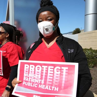 Nurse holds sign "Protect Nurses, Patients, Public Health"