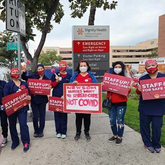 Nurses outside hospital hold signs "Staff Up for Safe Care"