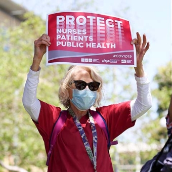 Masked nurse outside holds sign "Protect Nurses, Patients, Public Health