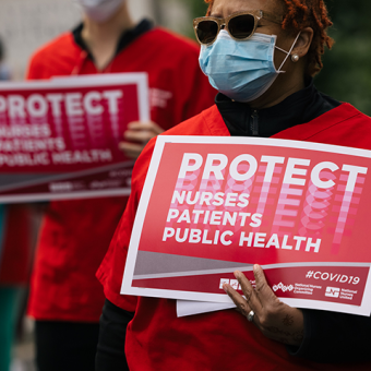 Nurses hold signs "Protect Nurses, Patients, Public Health"