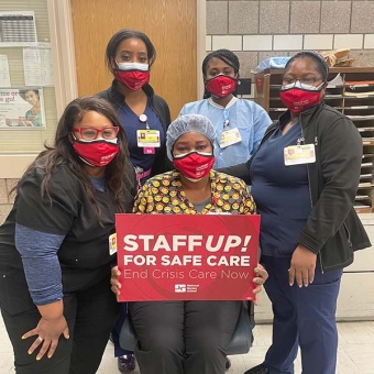 Group of nurses inside hosptial holds signs "Staff Up! For Safe Care"