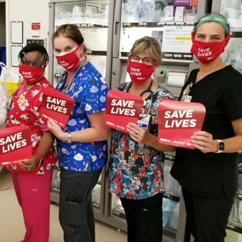 Nurses in hospital room holding "Save lives" signs