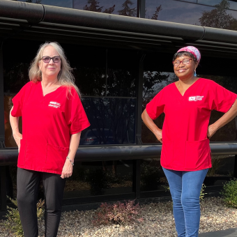 Two nurses outside in red scrub shirts