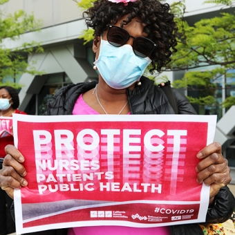 Nurse holding signs "Protect Nurses, Patients, Public Health"