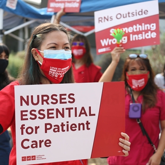 Nurse outside holds sign "Nurses essential for patient care"