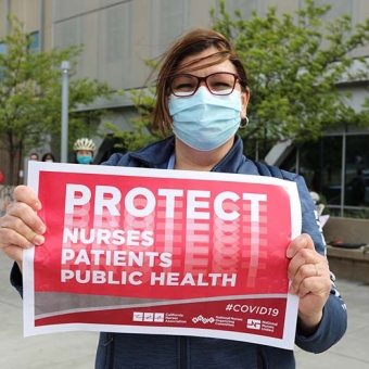 Nurse outside holds sign "Protect Nurses, Patients, Public Health"